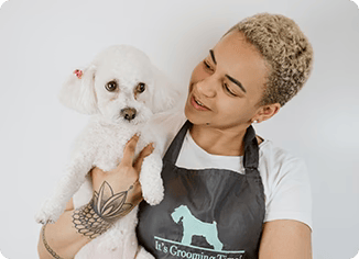 Dog groomer holding a groomed white poodle.